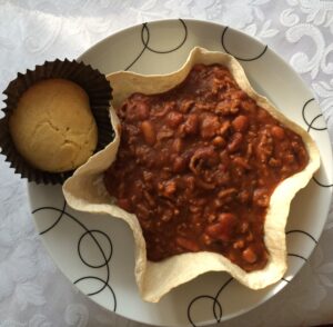 a bowl of chili and a muffin on a plate