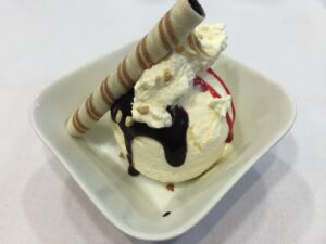 a bowl of ice cream with chocolate syrup and waffle roll