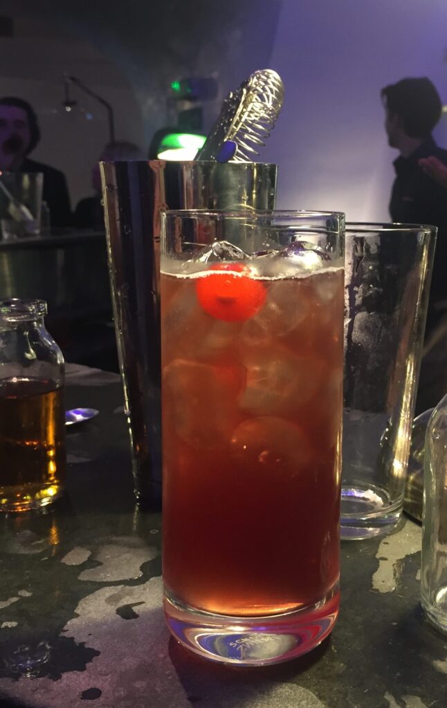 a glass of liquid with ice and a cherry on top