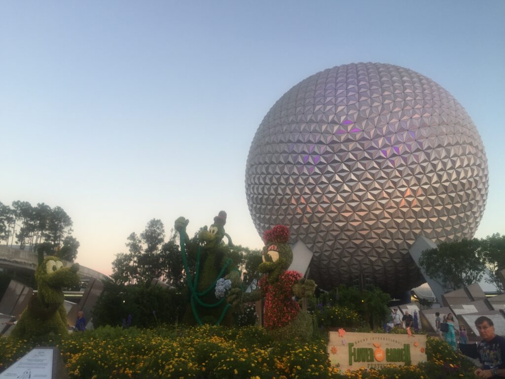 a large silver sphere with plants and a statue of mickey mouse