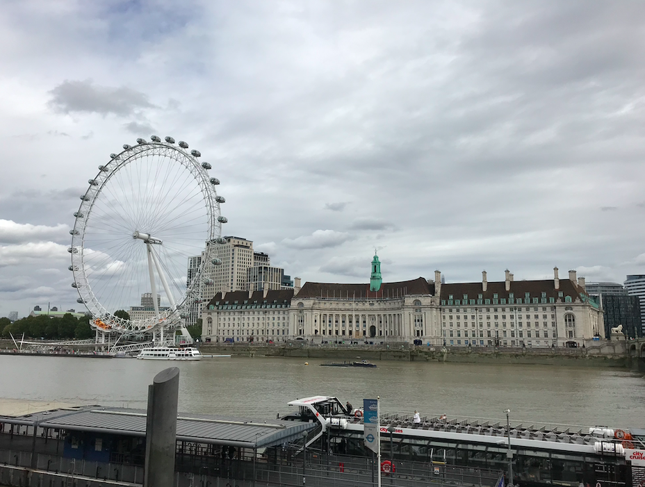 a large ferris wheel next to a river with London Eye in the background